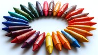 Vibrant crayons arranged in rainbow circular pattern on white background, creating colorful spectrum display for art, education and creativity concepts.