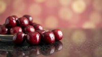 Fresh red cranberries spilling from glass bowl on dark surface with warm bokeh lights background for holiday cooking and festive seasonal recipes.