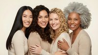 Four diverse women of different ages embracing and smiling together in neutral tones, representing friendship, sisterhood and multigenerational bonds.