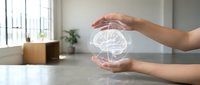 Hand protecting glowing brain hologram above desk, representing artificial intelligence, innovation, and technology protection in modern office environment.