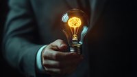 Business person holding glowing lightbulb with illuminated brain inside against dark background, representing innovation, creative thinking and bright business ideas.