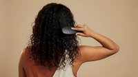 Woman with curly hair brushing locks with black comb for healthy hair care routine and styling maintenance.