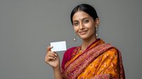 Young South Asian woman in traditional orange and red sari holding blank business card against gray background, showcasing cultural elegance in professional context.