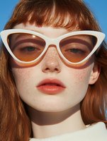 Young redhead woman with freckles wearing white cat-eye sunglasses against blue sky background. Summer fashion portrait with retro vintage style eyewear.
