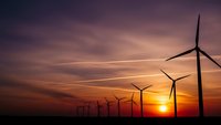 Wind turbines silhouetted against dramatic sunset sky with orange and purple clouds. Renewable energy concept for sustainable power generation and clean technology.