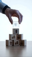 Hand placing a glass shield cube atop a pyramid of wooden blocks with security and finance icons, symbolizing protection and investment growth.