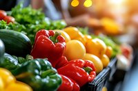 Fresh colorful bell peppers and vegetables in market display, vibrant red, yellow and green produce with natural lighting, selective focus on foreground peppers.
