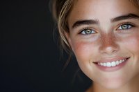 Close up portrait of young woman with freckles, bright blue eyes and natural smile against dark background, radiating happiness and confidence.