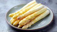 Fresh white asparagus spears arranged on gray ceramic plate, close up view showing tender stalks with pale yellow tips against dark background.