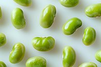 Fresh green edamame beans scattered on white background, showcasing vibrant color and glossy texture for food photography.