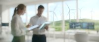 Two business professionals discussing documents in modern office with wind turbines visible through window representing renewable energy collaboration.