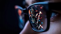 Close-up of eyeglasses reflecting colorful city lights at night, showing digital urban landscape in lens while revealing partial view of person's eye.