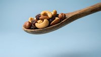 Mixed nuts and dried fruits on wooden spoon against blue background. Healthy snacking concept for nutrition and wellness content.