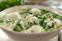 Homemade dumpling soup with tender dough balls, fresh herbs and green onions in clear savory broth served in white ceramic bowl. Perfect comfort food.