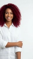 Confident African American businesswoman with burgundy curly hair smiling in white shirt against neutral background for professional headshot.