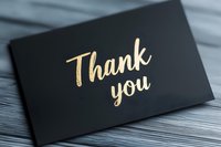 Elegant gold foil thank you text on black luxury card against textured wood surface, modern calligraphy style lettering for special occasions and events.