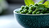 Fresh green peas in a textured bowl with mint leaves, ideal for food, cooking, nutrition, and healthy eating content.