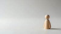 Single wooden peg figure standing alone on white surface against neutral background representing isolation, loneliness, minimalism and individual concept.