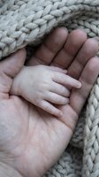 Newborn baby hand gently held in protective adult hands on soft knitted blanket. Tender moment capturing love, care and family bond in cozy setting.