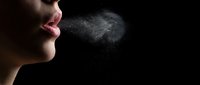 Young woman exhaling visible breath vapor in cold air against black background, showing respiratory droplets and moisture particles in dramatic lighting.