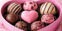 Assorted chocolate truffles and pralines in heart shaped pink box with romantic heart shaped candy, decorated with sprinkles and drizzles for Valentine's Day.