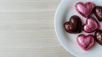 Heart-shaped chocolate candies wrapped in colorful foil on white plate over wooden table background for Valentine's Day celebration and romantic occasions.