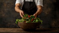 Professional chef preparing fresh green salad with colorful vegetables in rustic wooden bowl on dark background, dramatic food photography style.