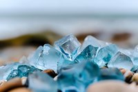 Luminous aqua blue crystal formation on natural stone background, macro photography showcasing transparent mineral structure and light refraction patterns.