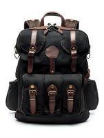 Black canvas backpack with brown leather straps and multiple front pockets, featuring brass buckles and adjustable shoulder straps for outdoor adventure and travel use.