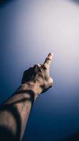 Male hand pointing upward with index finger against gradient blue sky background for motivation and direction concepts.