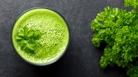 Fresh green smoothie with parsley garnish on dark surface, healthy detox drink for wellness and nutrition lifestyle.