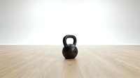 Black kettlebell weight on wooden floor in minimalist gym studio setting, suitable for fitness, training, and wellness design projects.