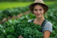 Young female farmer in straw hat holding fresh organic kale from garden. Natural green background showcases sustainable agriculture and farm-to-table lifestyle.