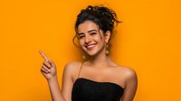 Young woman with curly updo hairstyle smiling and pointing finger against vibrant orange background, wearing strapless black top for fashion and beauty advertising.