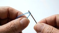 Close-up of hands threading a blue thread through a needle eye, sewing concept on white background.