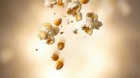 Flying popcorn kernels scattered in air against warm golden background, snack food concept for cinema entertainment and movie theater advertising.