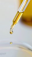 Close-up macro shot of golden oil drop falling from glass pipette or dropper against blurred background, showing liquid viscosity and transparency in cosmetic lab.