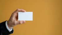 Close-up of male hand holding blank white business card against golden yellow background. Professional networking and corporate identity concept for branding.