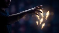 Hand holding glowing sparkler sticks with golden light particles and sparks against dark blurred background for celebration and festive events.
