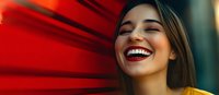 Young Hispanic woman with bright authentic smile and closed eyes against vibrant red background, wearing yellow top. Natural joyful expression captures genuine happiness.