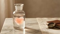 Glass bottle with pink heart inside on marble surface with vintage sunglasses, romantic love concept for Valentine's Day greeting cards and gifts.