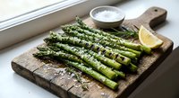 Grilled asparagus spears with herbs and lemon on rustic wooden cutting board. Fresh green vegetables prepared for healthy meal or side dish.