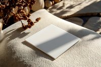 Blank white paper on textured fabric with dried flowers casting natural shadows in warm sunlight, minimalist composition for creative design mockup.