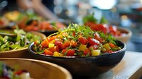 Fresh colorful salad with diced tomatoes, yellow bell peppers, and mixed greens garnished with microgreens served in dark ceramic bowl on restaurant table.