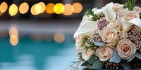 Elegant bridal bouquet with blush roses and white calla lilies against blurred bokeh lights and turquoise water, creating romantic wedding atmosphere.