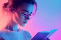 Young Asian woman in round glasses reading book under neon lighting, profile view against gradient pink and blue background, wearing white fluffy sweater.