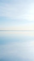 Serene lake or ocean horizon with calm water reflecting soft blue and white sky, suitable for backgrounds and wellness designs.