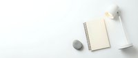 Minimalist workspace with open spiral notebook, white lamp and decorative stone on clean white background for office design and productivity concepts.