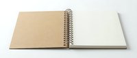 Open spiral-bound notebook with blank kraft paper and white pages on clean background for creative projects and note-taking applications.