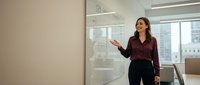 Professional businesswoman presenting data analytics on whiteboard in modern office conference room for corporate training and strategic planning sessions.
